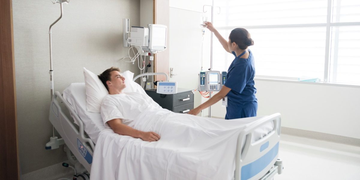 Young man in hospital being cared for by nurse. Medical professional looking after patient on hospital ward. Adjusting iv line, medication, care, bedside manner.