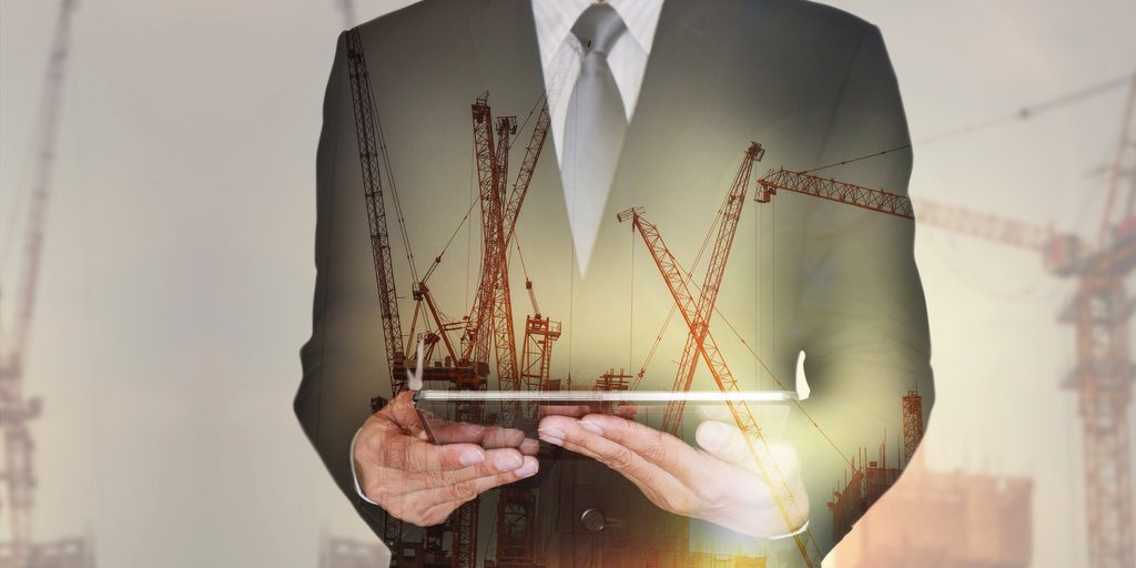 665721386 Double exposure of businessman hand hold tablet, construction crane, building and sunset in the evening as business, technology, communication and industry concept.